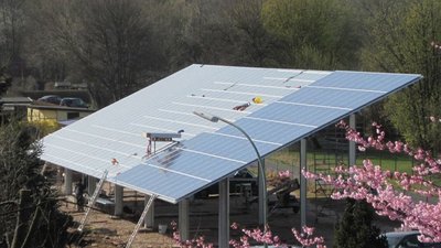 Ein großes Solarpanel-Dach steht auf einem Gerüst, umgeben von blühenden Kirschbäumen und einer grünen Landschaft.