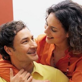 Ein lächelndes Paar sitzt eng beieinander, während sie sich liebevoll in die Augen schauen und eine warme Verbindung teilen.