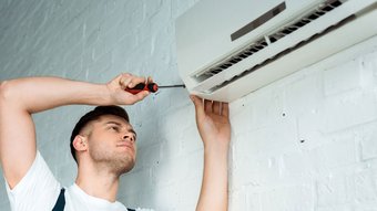 Ein Mechatroniker der an einer Klimaanlage schraubt
