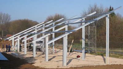 Eine Baustelle mit einem unvollendeten Gebäude, das aus Stahlträgern und -stützen besteht, umgeben von Bäumen und einem blauen Himmel.